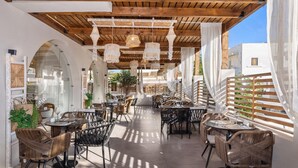 An outdoor café with wicker furniture, wooden beams, and hanging light fixtures.