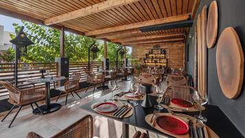 An outdoor dining area with wooden tables and chairs, surrounded by a wooden pergola.
