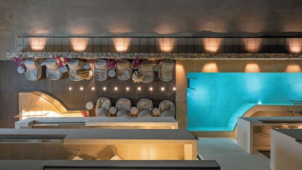 A modern spa area with a stone wall, seating, and a blue-tiled pool.
