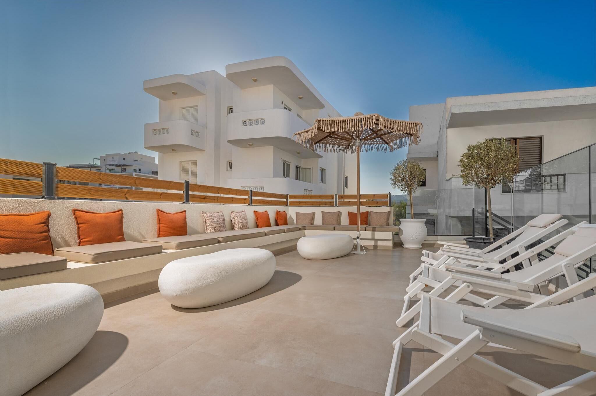 A rooftop terrace with white lounge chairs, orange cushions, and a large umbrella.