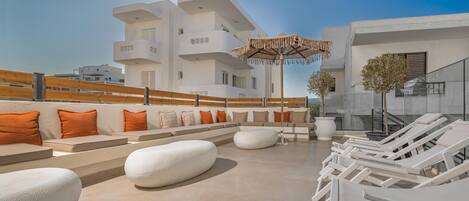 A rooftop terrace with white lounge chairs, orange cushions, and a large umbrella.