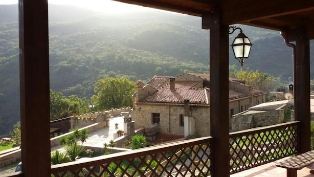 A stone building with a tiled roof, a wooden balcony with a lattice railing, and a view of a green valley. - Masseria rocca di Gonato (Castelbuono)