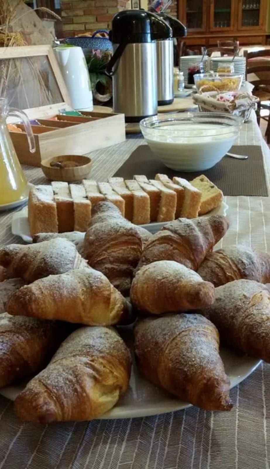 Una tavola imbandita per la colazione con pane, croissant e una ciotola di yogurt.