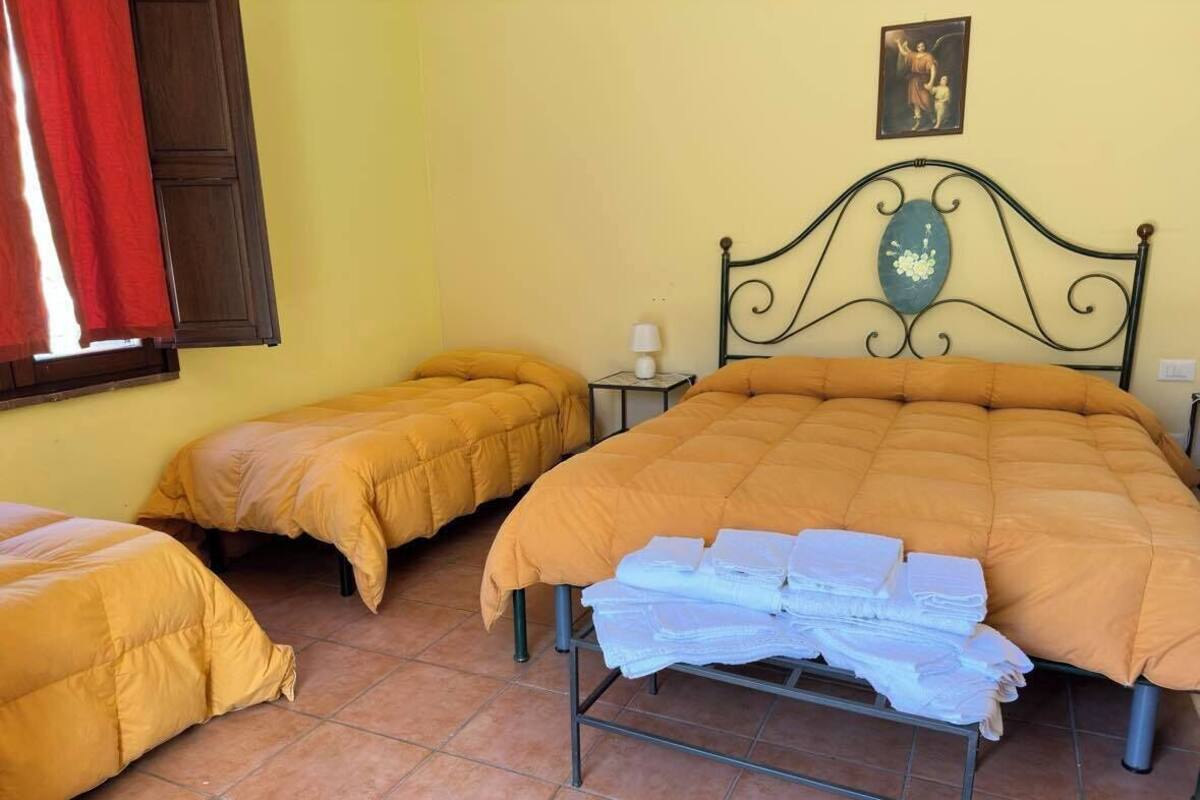 A room with two beds, each with a yellow duvet, a metal headboard, and a small bedside table with a lamp.