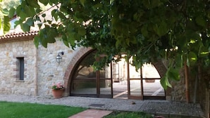 A stone building with a large arched doorway, a potted plant, and a pathway leading to the entrance. - Masseria rocca di Gonato (Castelbuono)