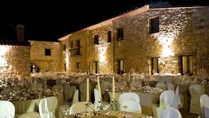 An outdoor dining area with stone buildings and tables set for a formal event. - Masseria rocca di Gonato (Castelbuono)