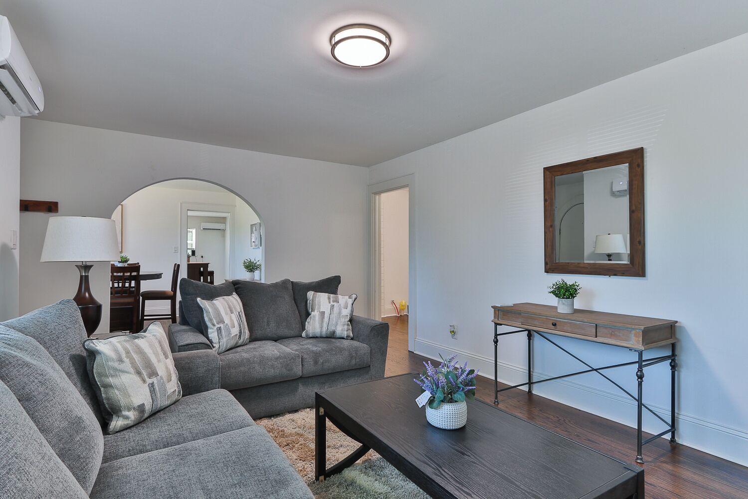Un salon avec un canapé gris, une table basse et une console surmontée d’un miroir.