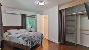 Quarto com cama, mesa de cabeceira, ar condicionado, janela com cortinas e closet espaçoso.