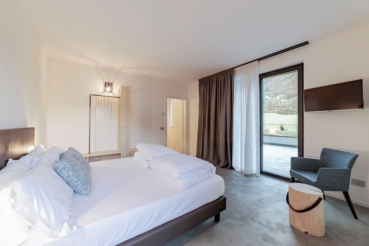 Una habitación de hotel moderna con una cama grande, un área de estar, un televisor y vistas al exterior.