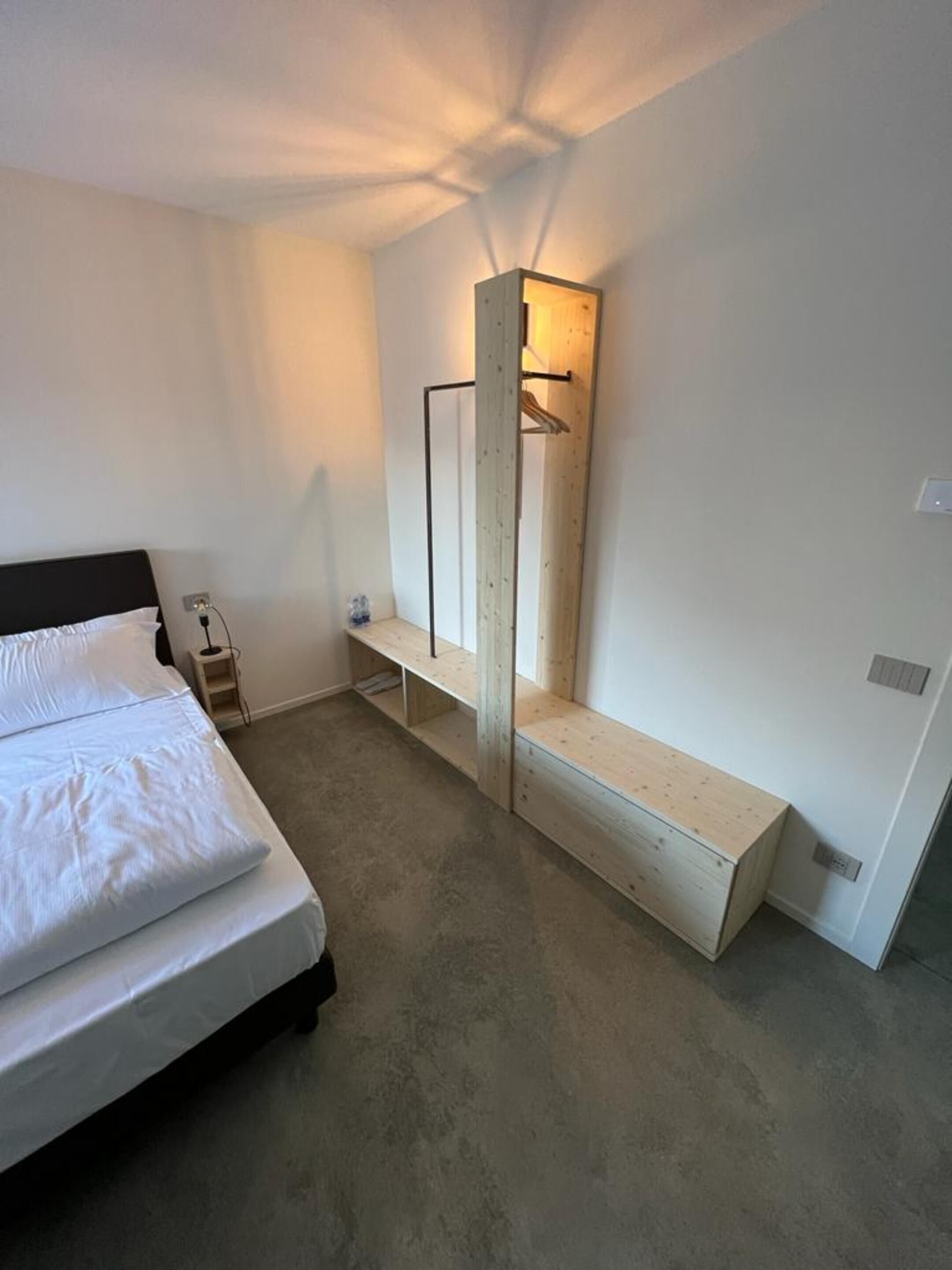 Un dormitorio con cama, un banco de madera, un espejo y una lámpara colgante.