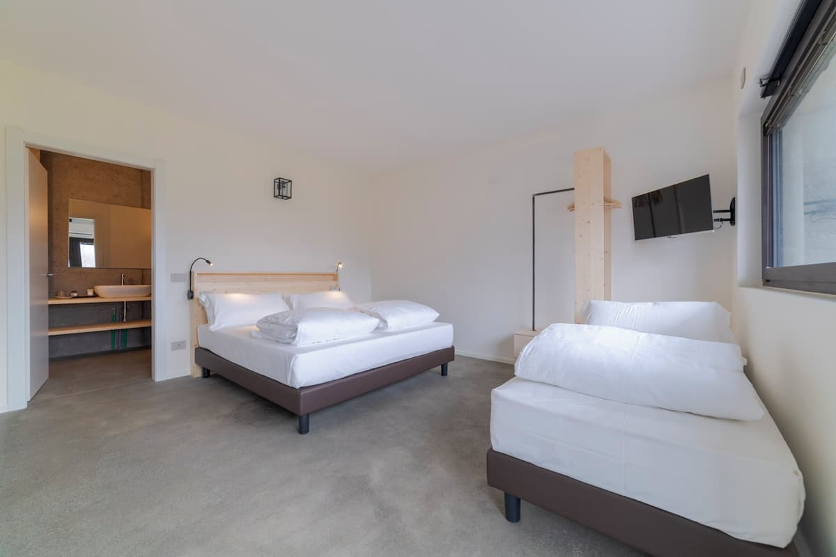 Un dormitorio moderno con una cama grande, un sofá más pequeño, un televisor montado en la pared y una unidad de estanterías empotrada.