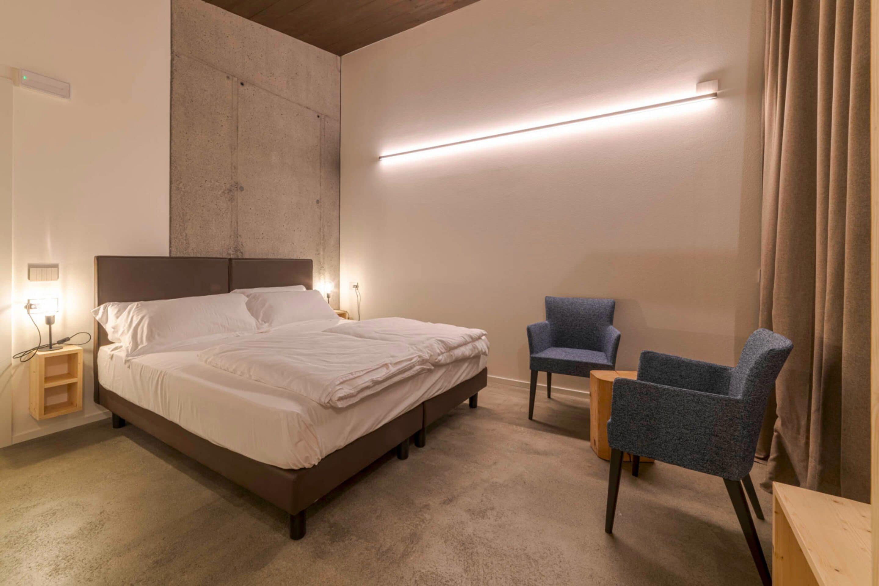 A bedroom with a bed, bedside tables, a chair, and a wall-mounted light fixture.