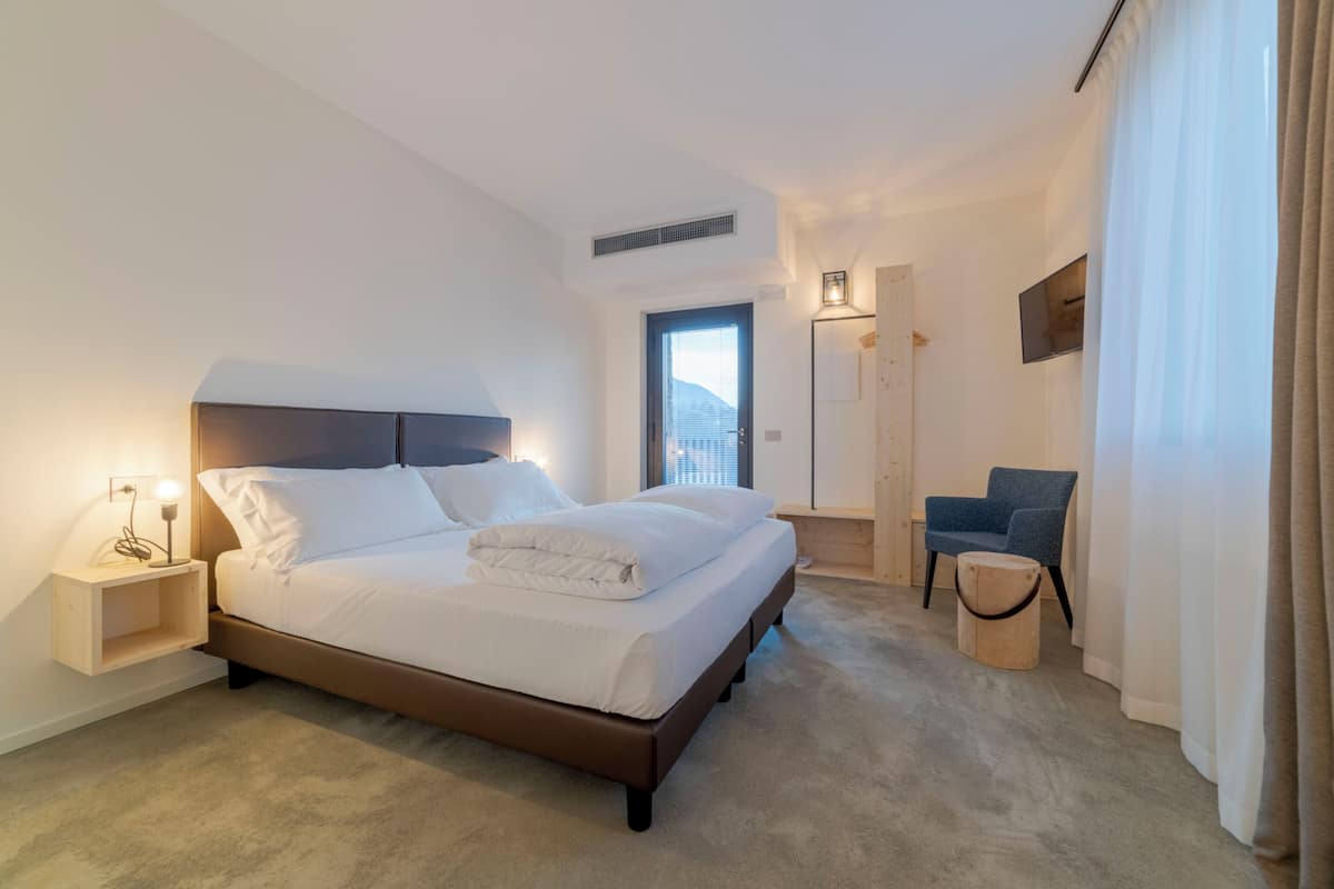 Un hotel moderno con una cama grande, mesitas de noche, una silla y vistas a la ciudad.