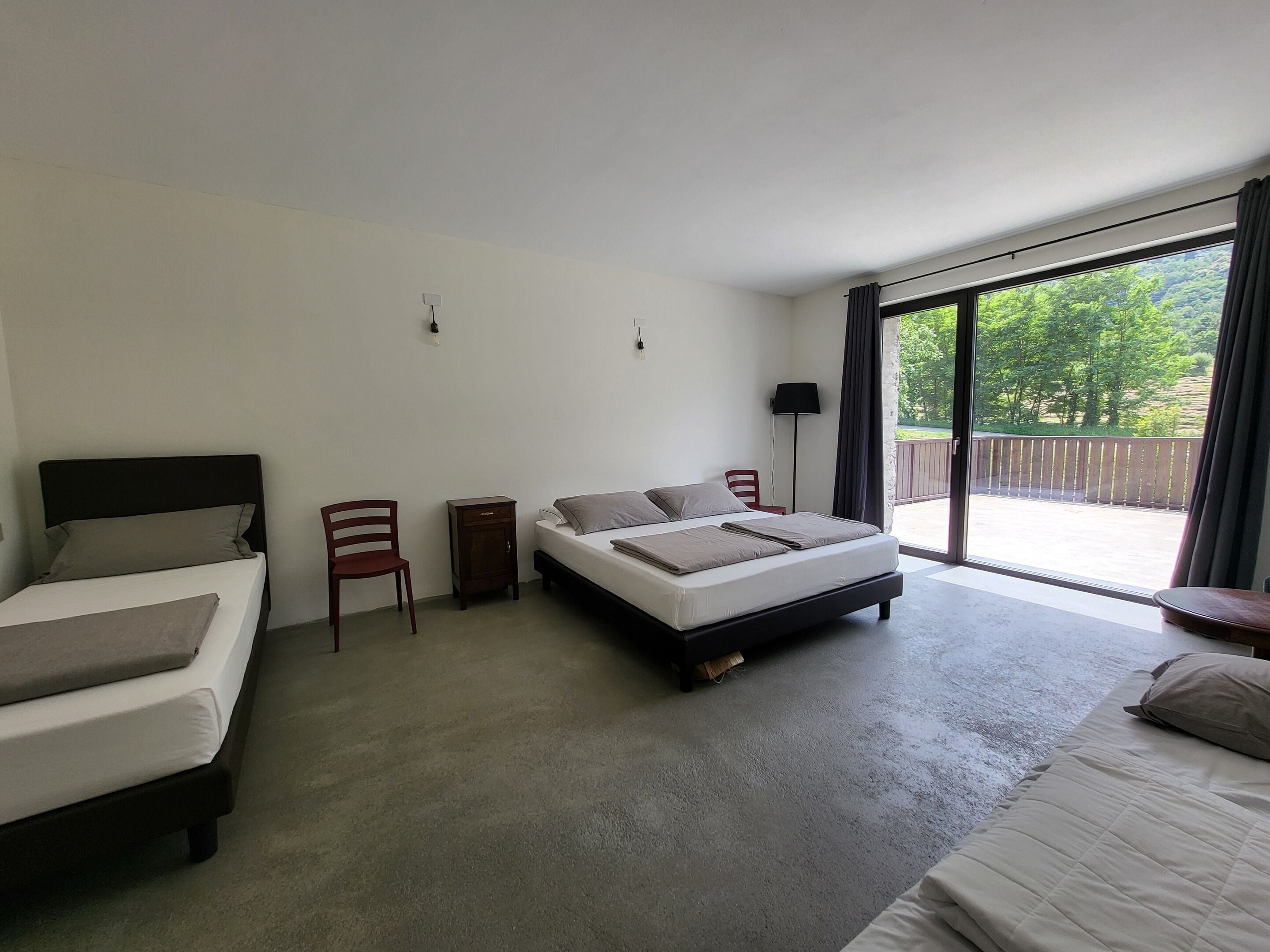 A hotel room with two beds, a small table, a chair, and a large sliding glass door leading to an outdoor area.