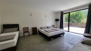 A hotel room with two beds, a small table, a chair, and a large sliding glass door leading to an outdoor area.