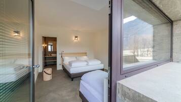 A modern hotel room with a large window, a bed, a bedside table, and a small seating area.