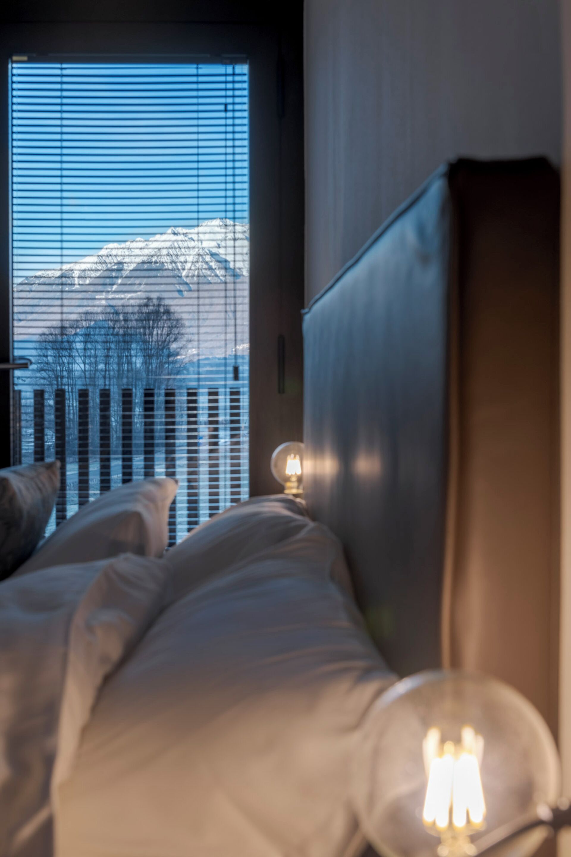 Ein Schlafzimmer mit Bett, Nachttisch und Fenster mit Blick auf schneebedeckte Berge.