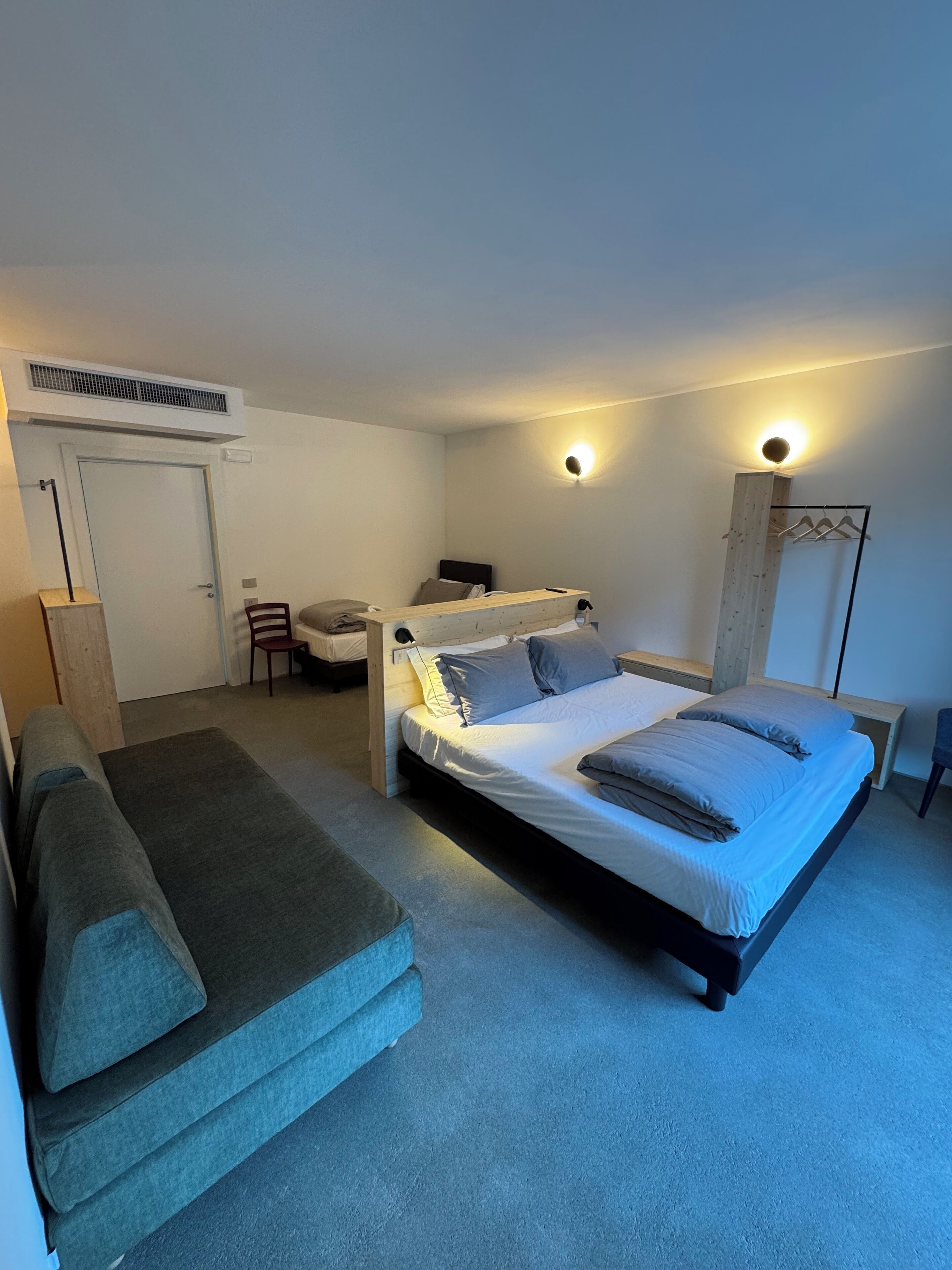 Quarto compacto com cama, escrivaninha pequena, cadeira e sofá.