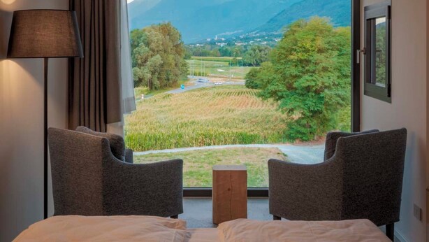Une chambre dotée d’une grande fenêtre donnant sur les montagnes, de deux fauteuils, d’une table de chevet et d’une lampe.