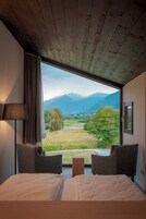 Un dormitorio con un ventanal que ofrece vistas a la montaña, dos sillas, una mesita de noche y una lámpara.