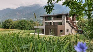Une maison moderne à deux étages, dotée d’une façade en pierre, de grandes fenêtres et d’un escalier apparent.
