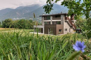Una casa moderna de dos pisos con fachada de piedra, ventanas grandes y una escalera visible.