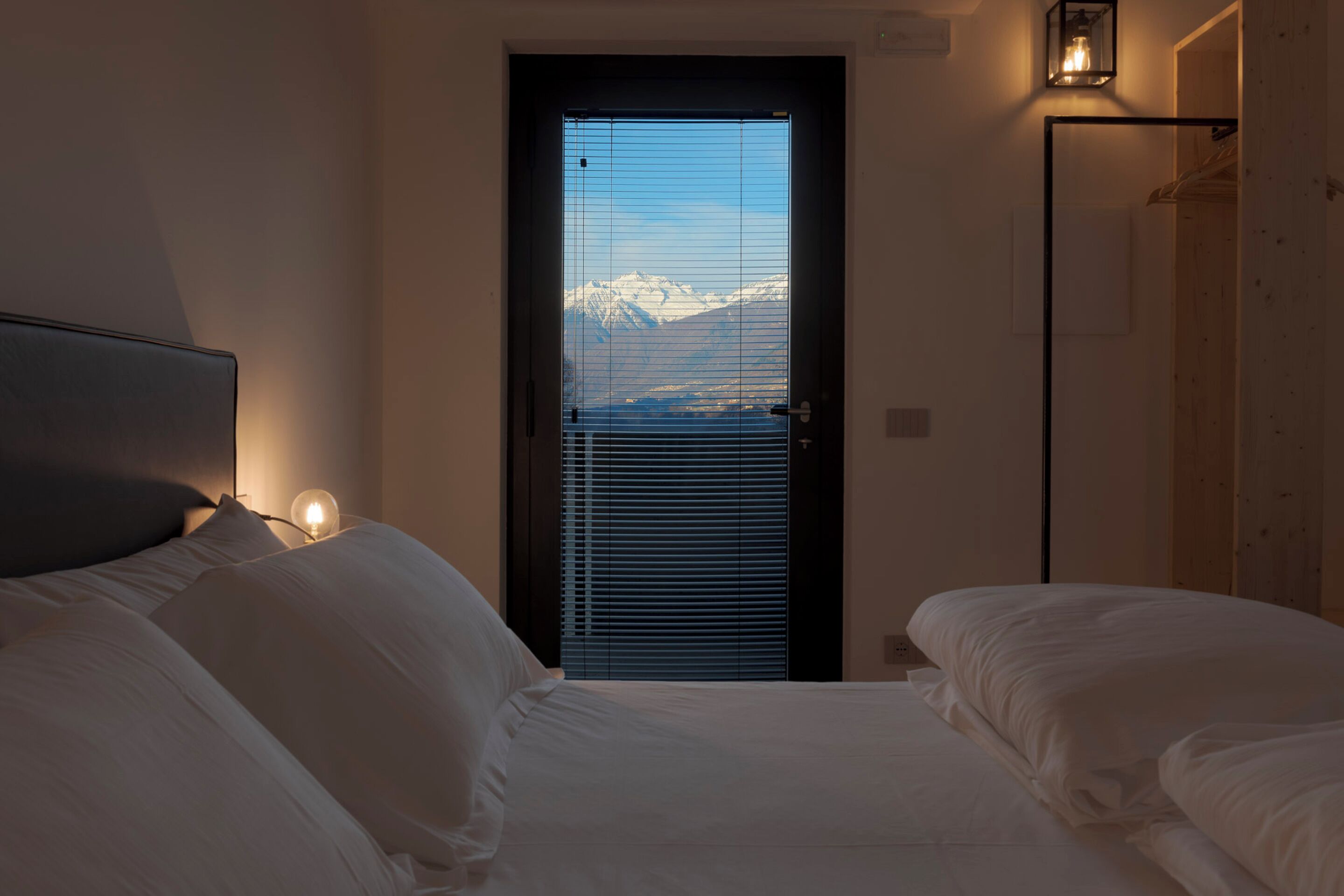 Ein Schlafzimmer mit Bett, einer Tür mit Blick auf schneebedeckte Berge und einer Wandleuchte.