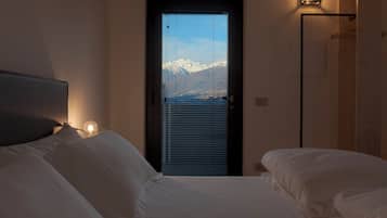 Ein Schlafzimmer mit Bett, einer Tür mit Blick auf schneebedeckte Berge und einer Wandleuchte.