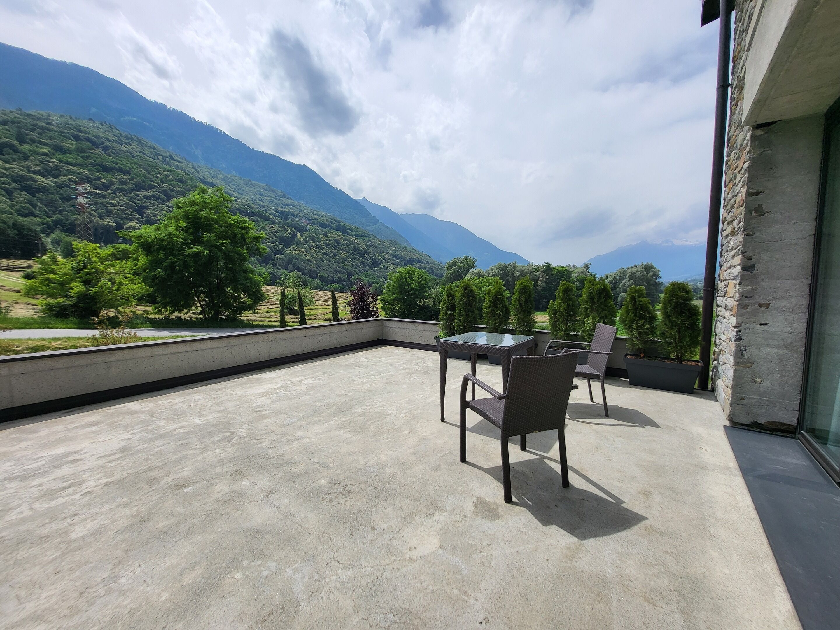 A balcony with a table and chairs, overlooking a mountainous landscape.
