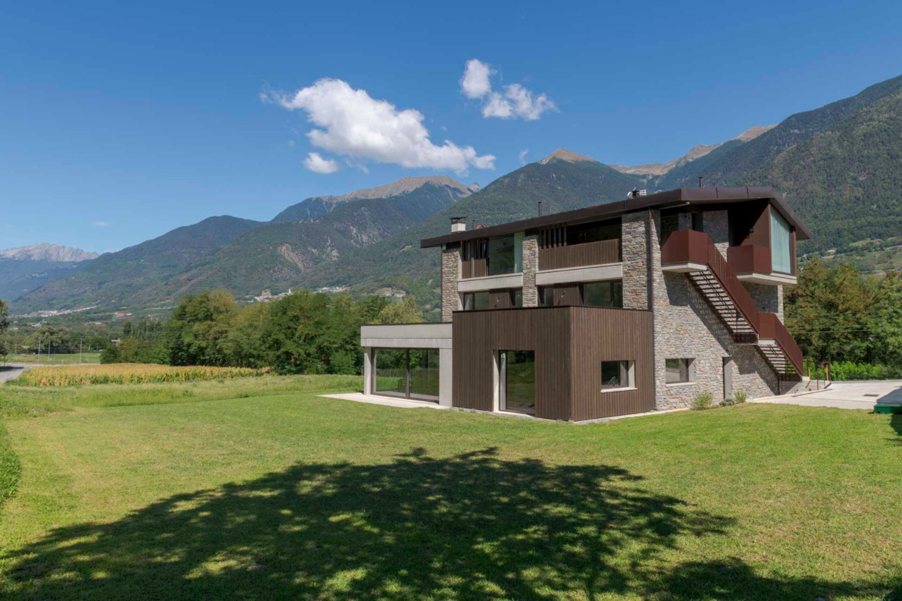 Ein modernes, zweistöckiges Haus mit einer Stein-Fassade, großen Fenstern und einer Treppe, die zum Obergeschoss führt.