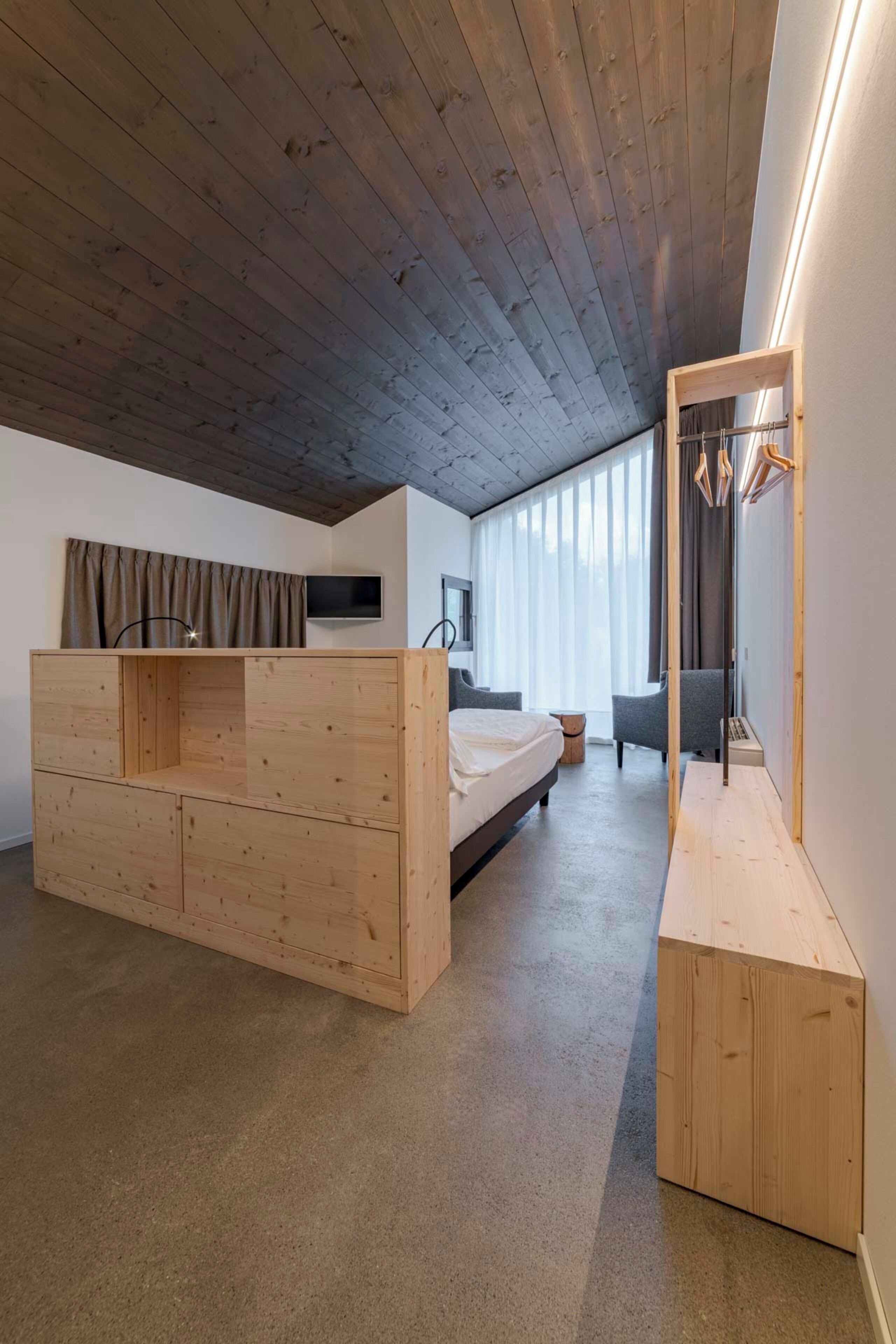 Un dormitorio con cama de madera, televisor, espejo y ventana con cortinas.