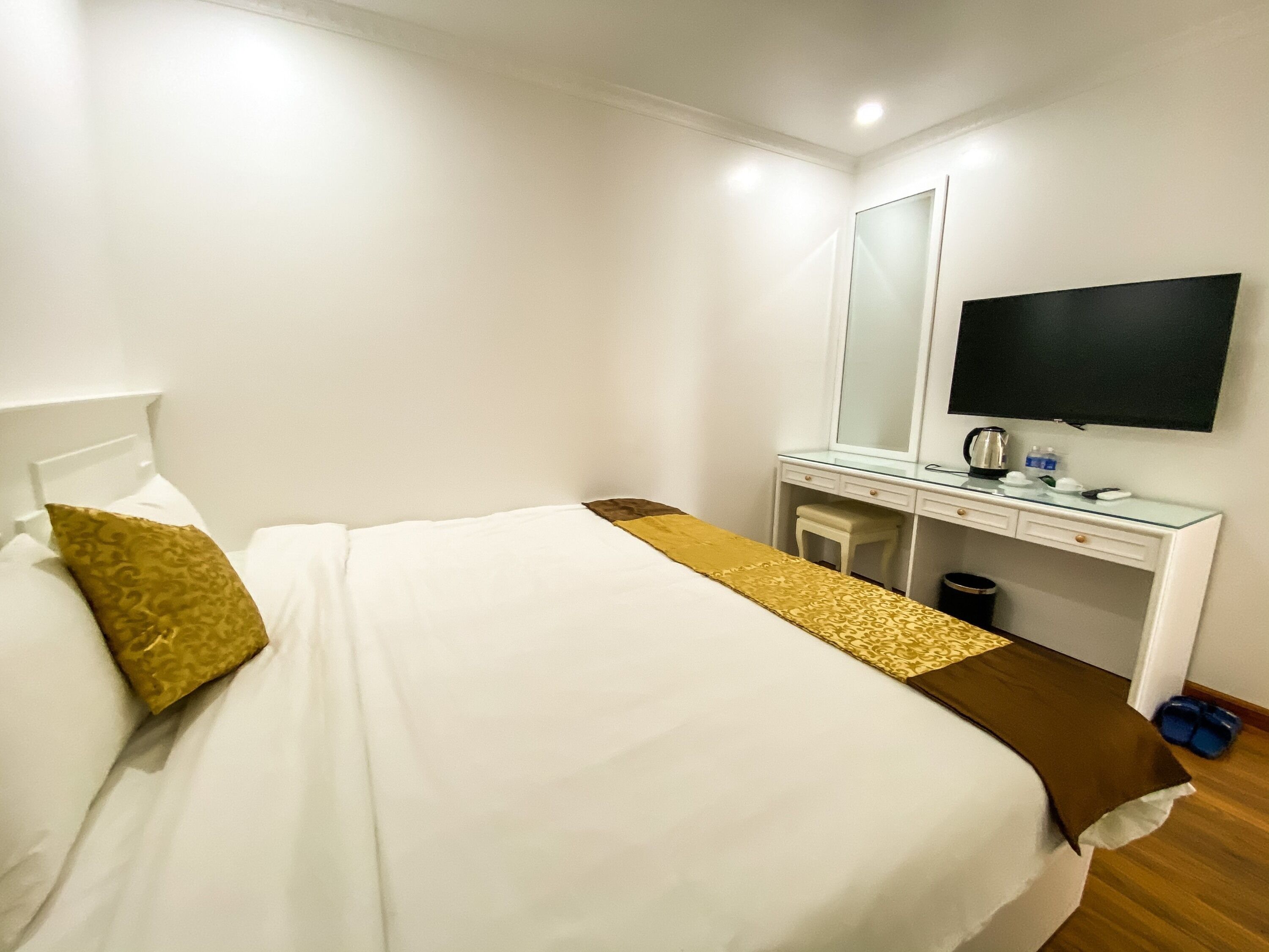 A hotel room with a bed, a desk, a mirror, a television, and a trash bin.