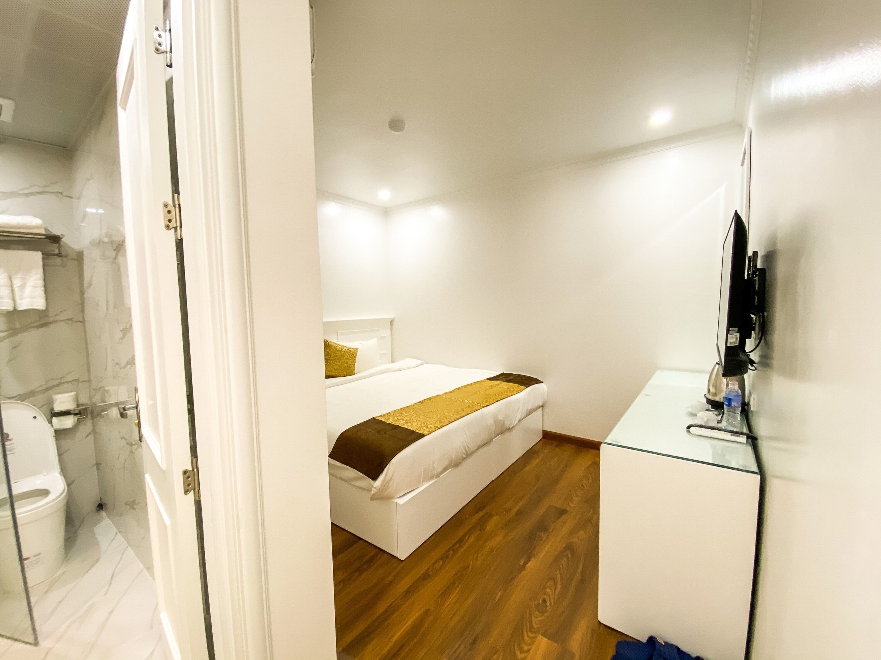 A hotel room with a bed, a small desk, a television, and a bathroom visible through an open door.