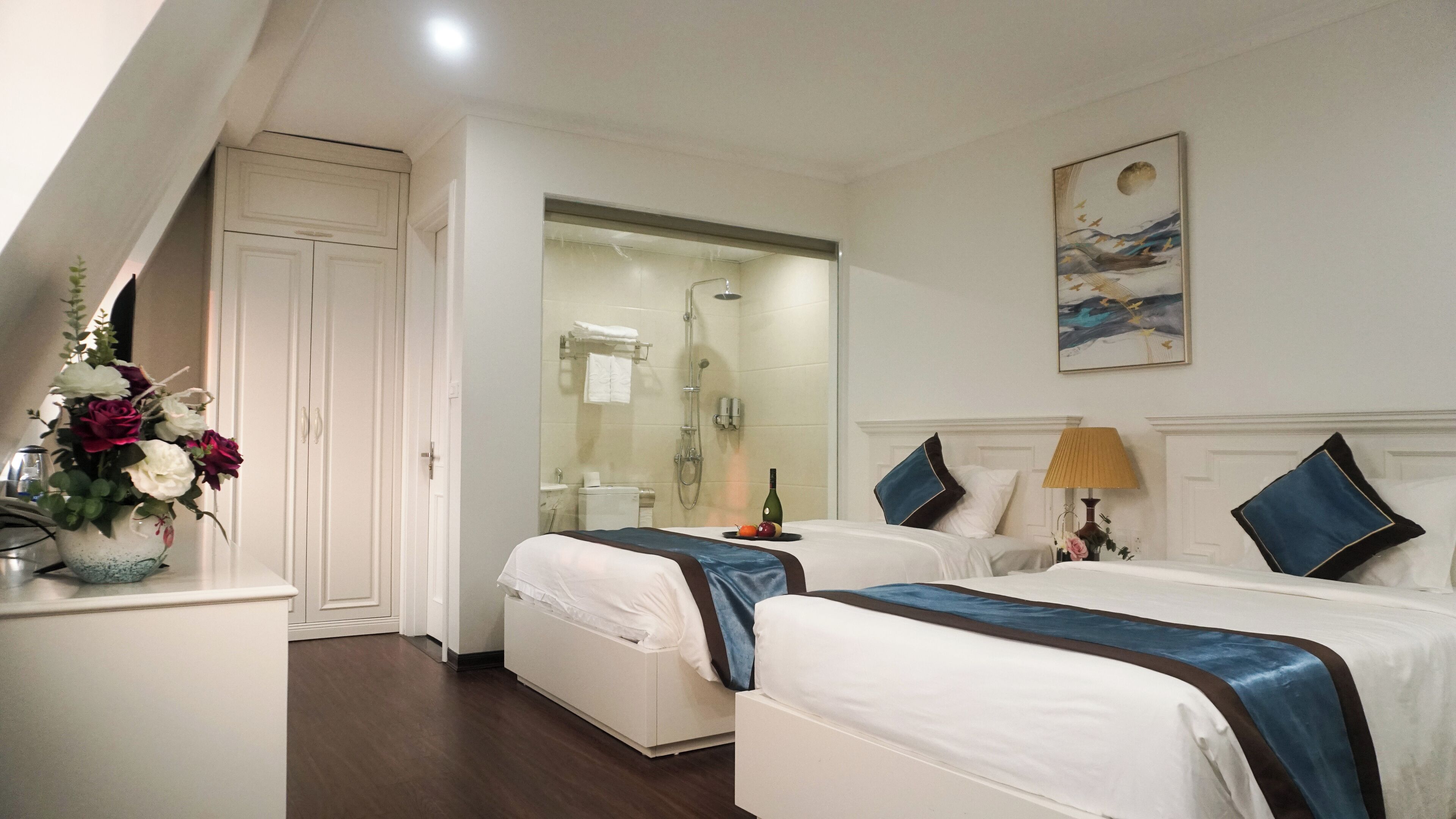 Una habitación de hotel con dos camas, ducha, baño y un cuadro en la pared.
