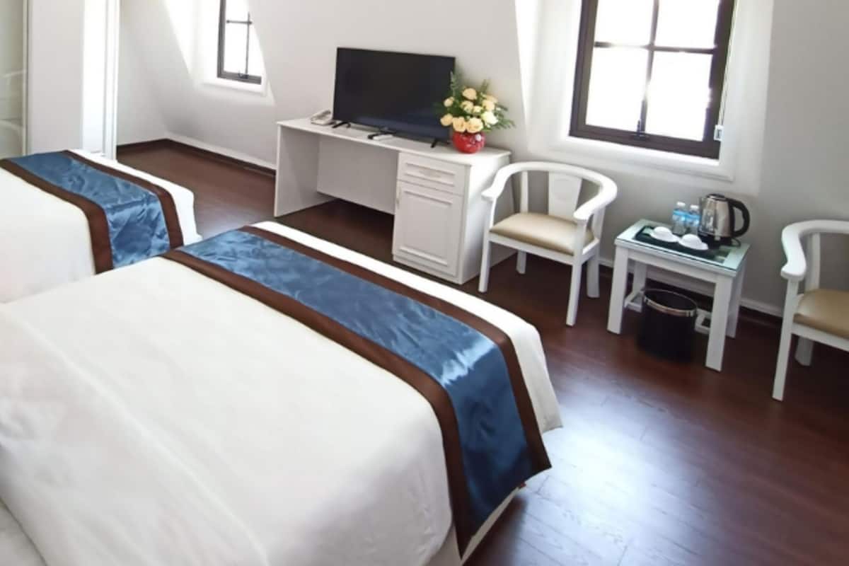 Una habitació d'hotel amb dos llits, un escriptori, una cadira, un televisor i una taula petita amb un vas de flors.