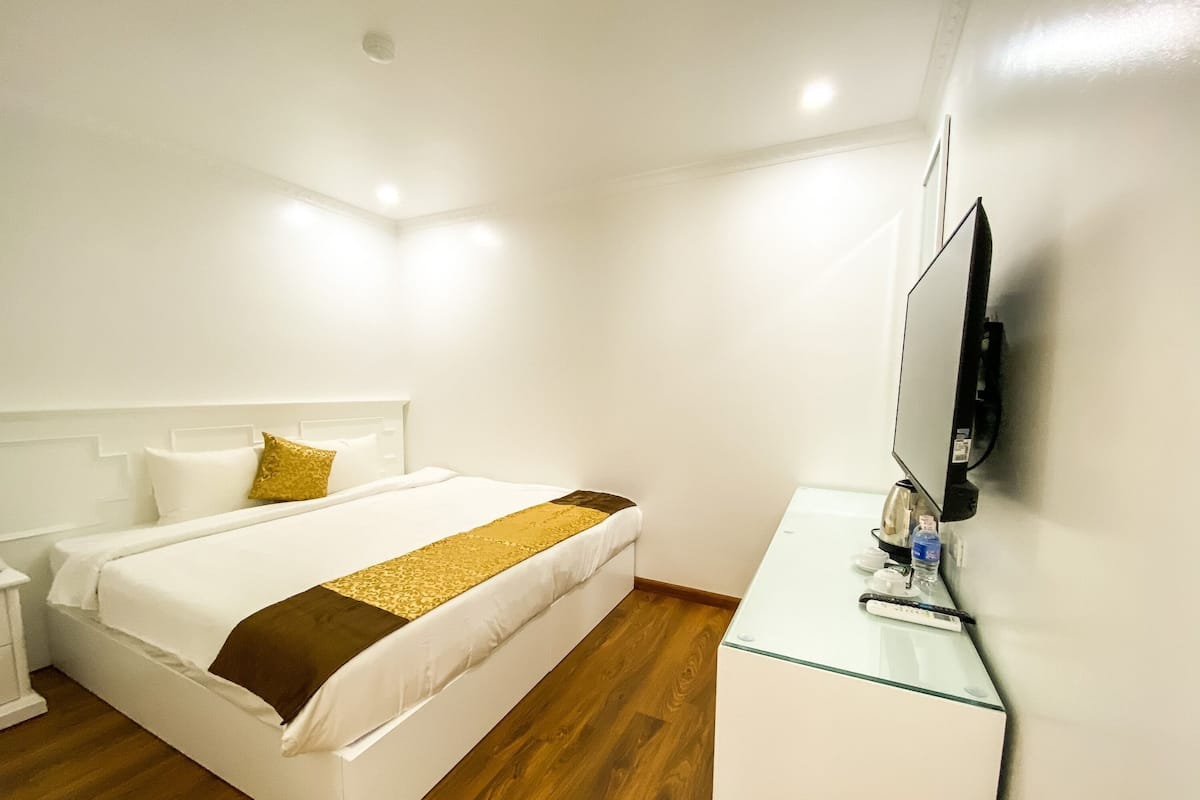 Habitació d'hotel amb llit, taulell de nit i televisió plana penjada a la paret.