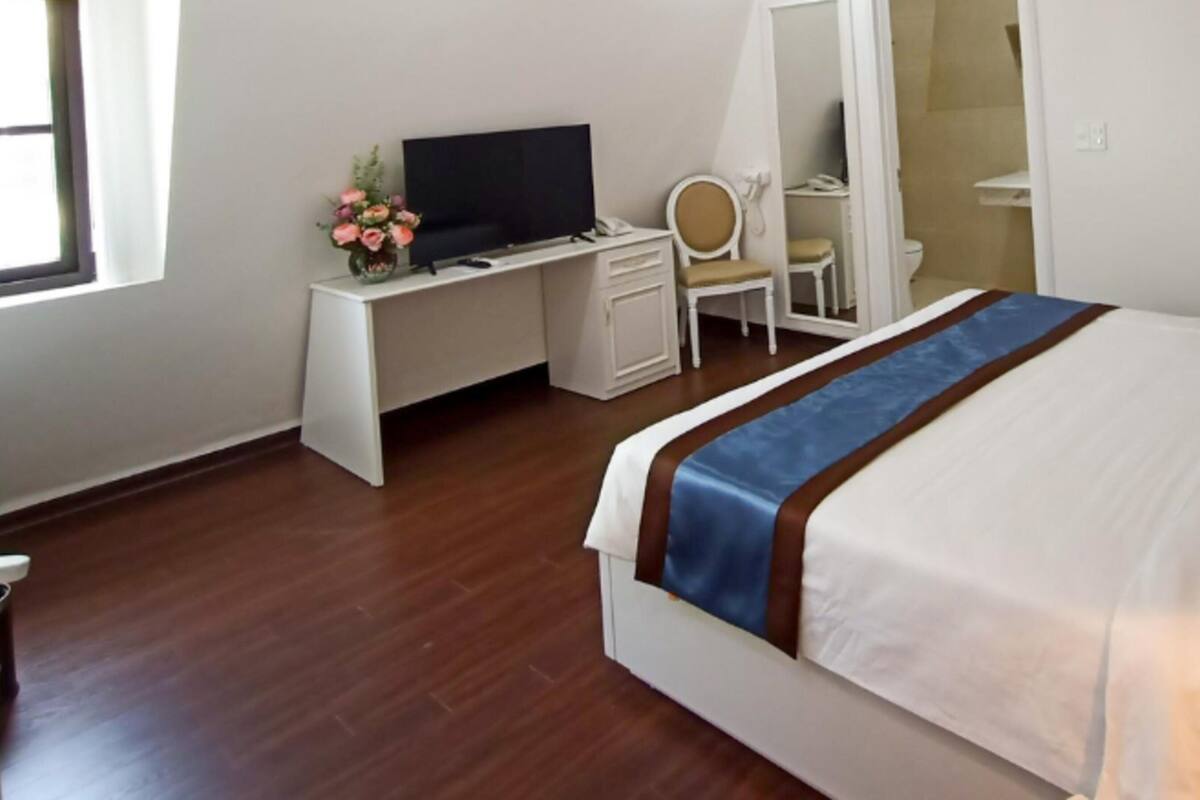 Habitació d'hotel amb un llit, una taula de nit amb televisió, una cadira i un mirall.