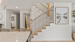 Un intérieur moderne avec un escalier, un coin repas et un tableau encadré au mur.