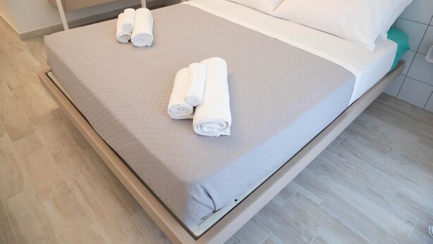 Un lit bien fait, avec deux serviettes enroulées, et un plancher en bois propre, de couleur claire.