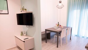 Une chambre moderne dotée d’un téléviseur à écran plat fixé au mur, d’un petit bureau avec une télécommande, d’une table à manger avec des chaises et d’un luminaire suspendu.