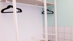 Une salle de bain avec un mur recouvert de carreaux blancs, une étagère en bois et deux cintres noirs sur un porte-manteau blanc.