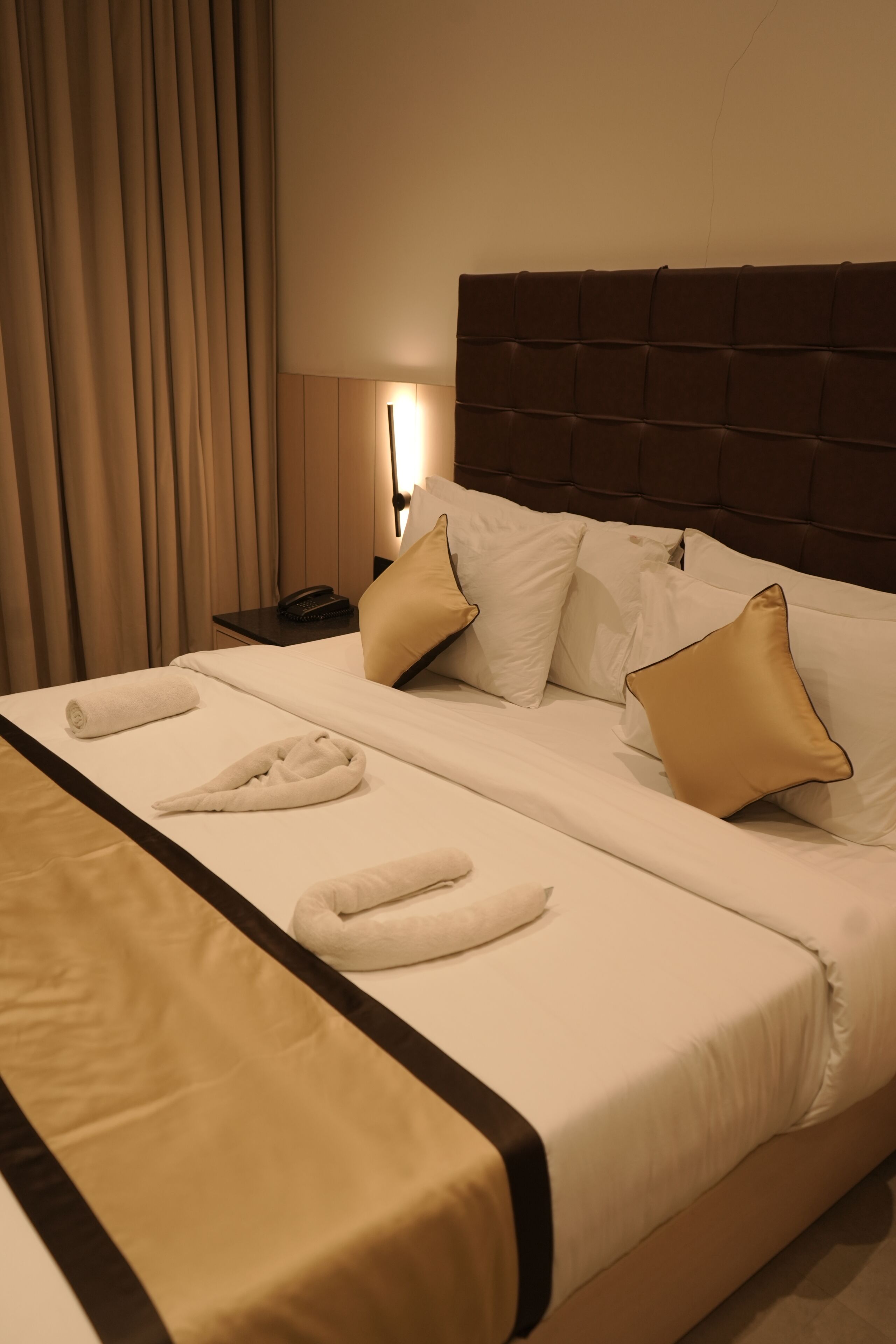 A neatly made bed with white linens, two gold pillows, and two white towels folded on the bed.