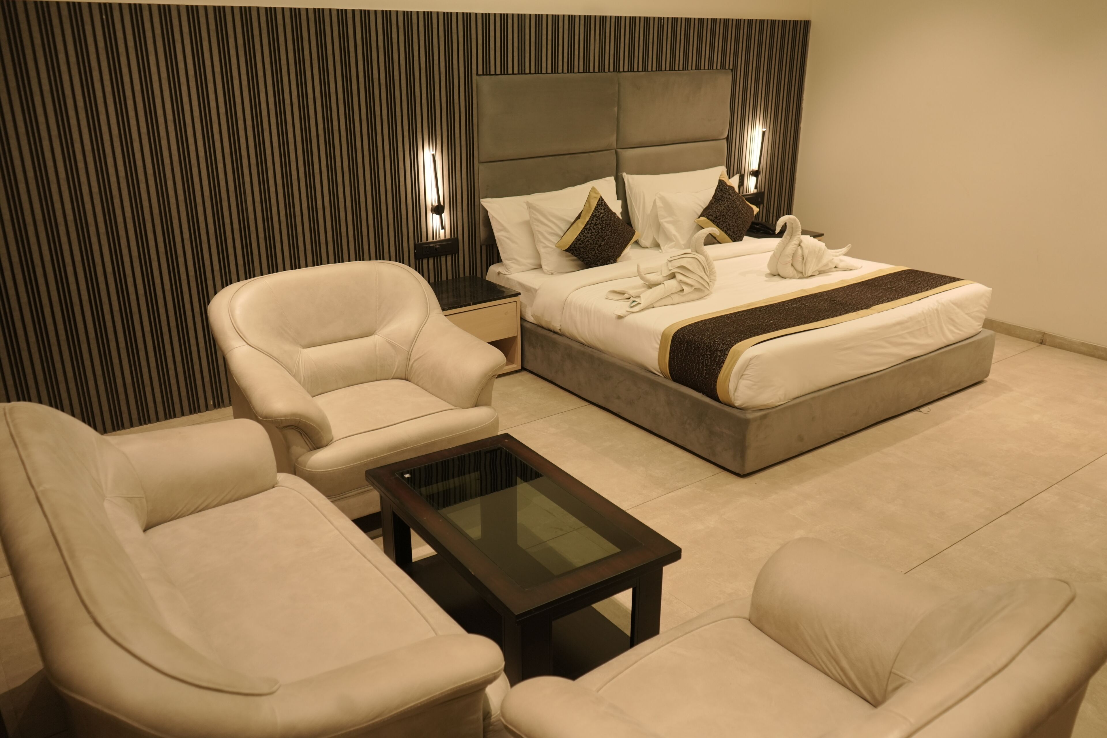 Een hotelkamer met een bed, twee fauteuils, een salontafel en een gestreepte wand.
