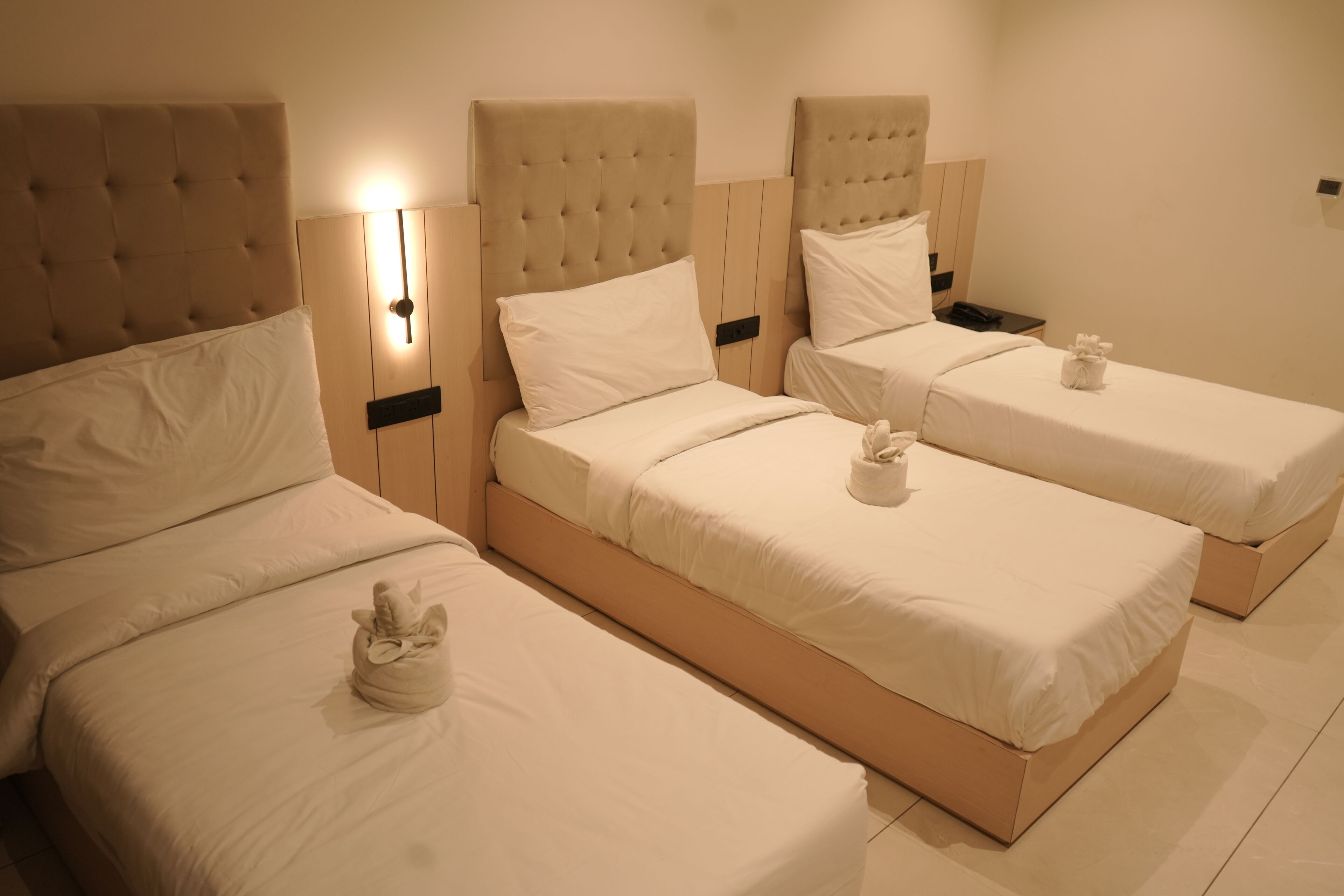 A hotel room with three beds, each with a headboard and a bedside table.