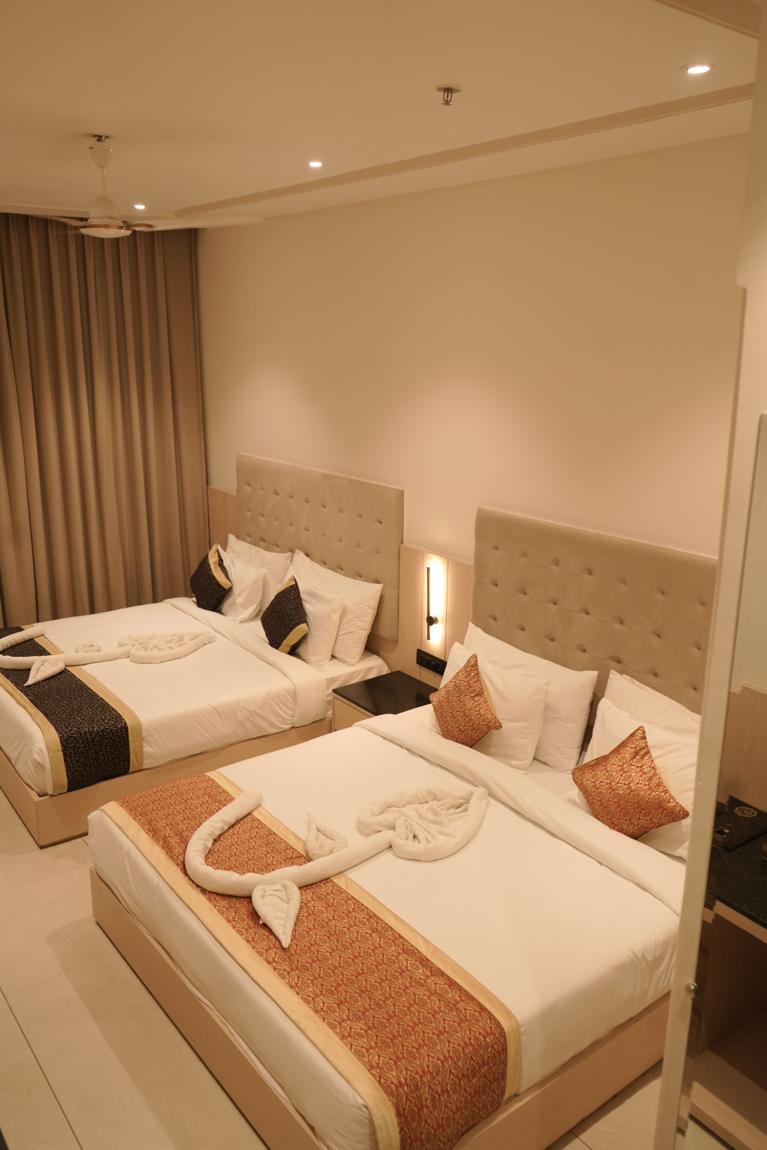 A hotel room with two beds, beige headboards, white bedding, and a large window with curtains.