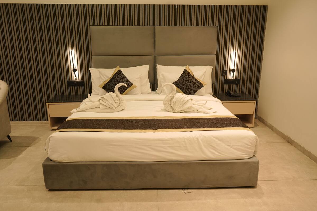 Een keurig opgemaakt bed met hoofdbord, twee nachtkastjes en een muur met verticale strepen.