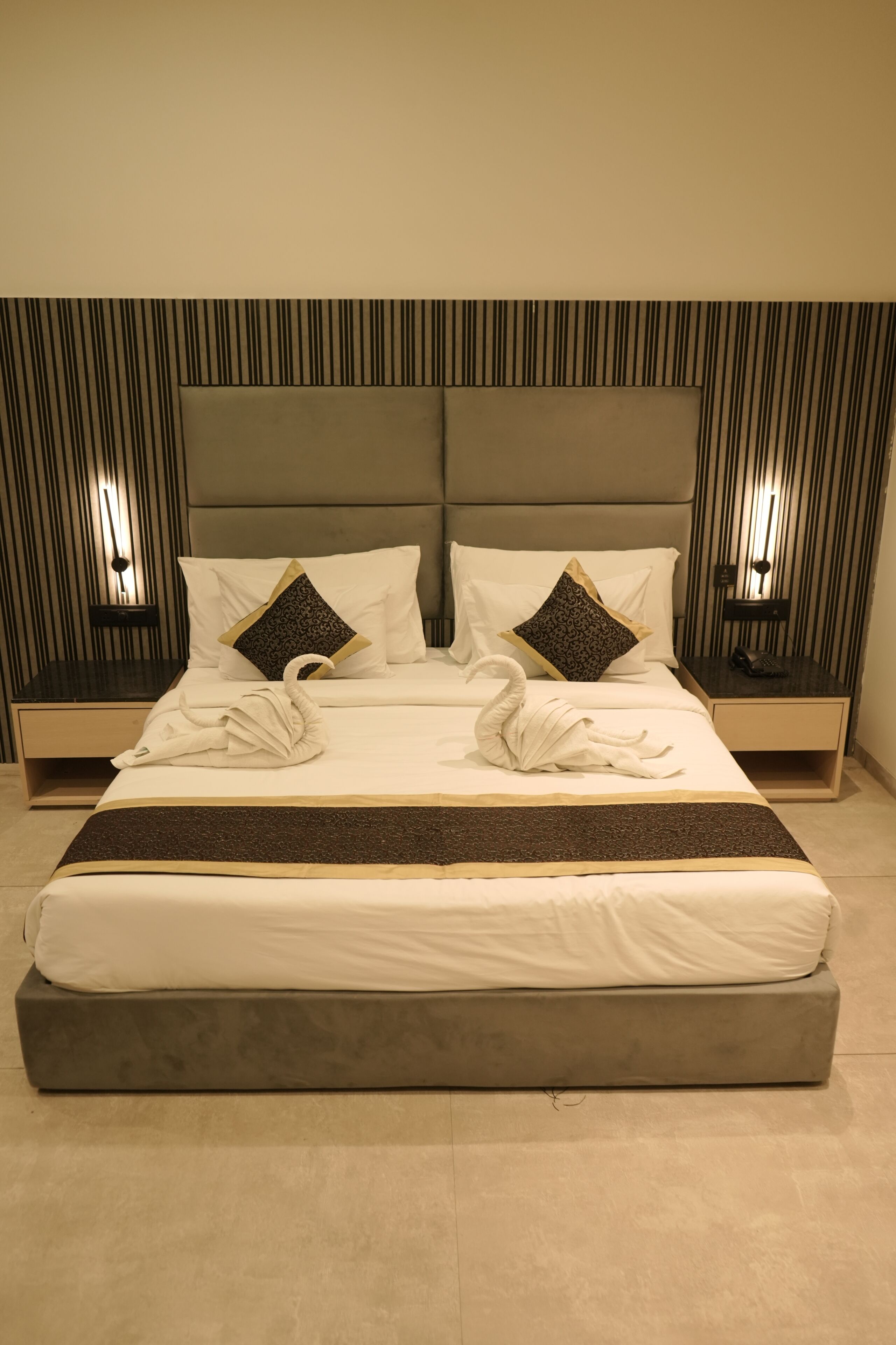 A neatly made bed with a large pillow and a decorative swan towel arrangement.