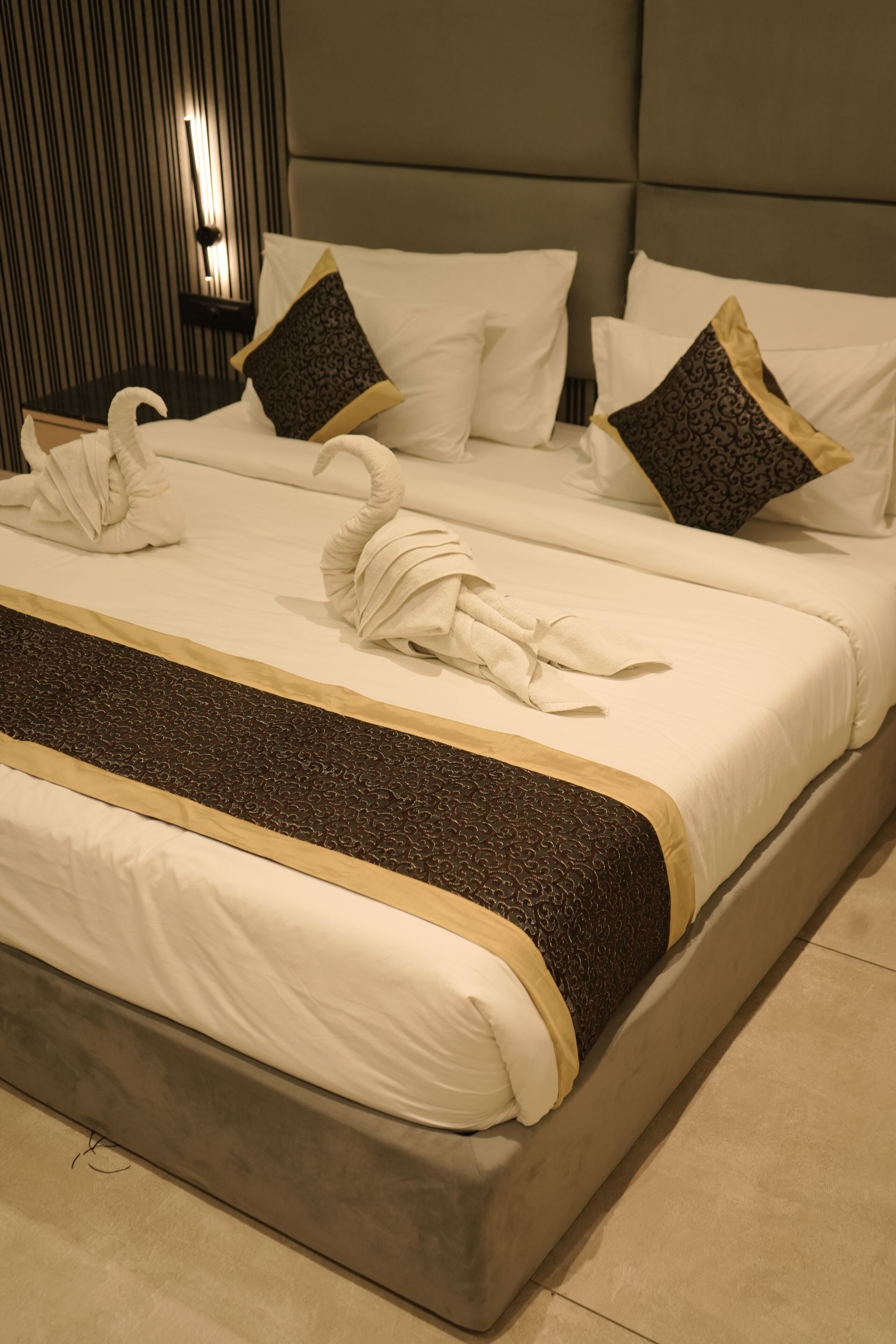 A hotel room with a large bed, two pillows, and a decorative towel arrangement.