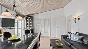 Una sala de estar moderna con una mesa de comedor de madera oscura, un sofá de cuero negro y una zona de cocina con un aparador de vidrio y un televisor.