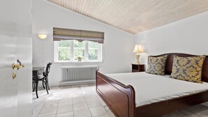 Un dormitorio con cama de madera, radiador, ventana con cortinas, escritorio con silla y lámpara.